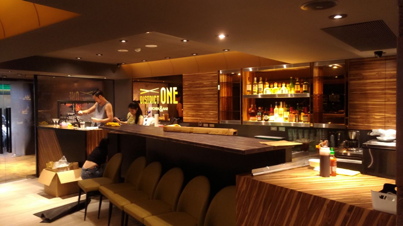 商業空間吧台區以深黑色與紋理木皮為基底，結合不鏽鋼發光酒櫃展示架與弧形間接照明天花，營造沉穩俐落的餐飲氛圍。