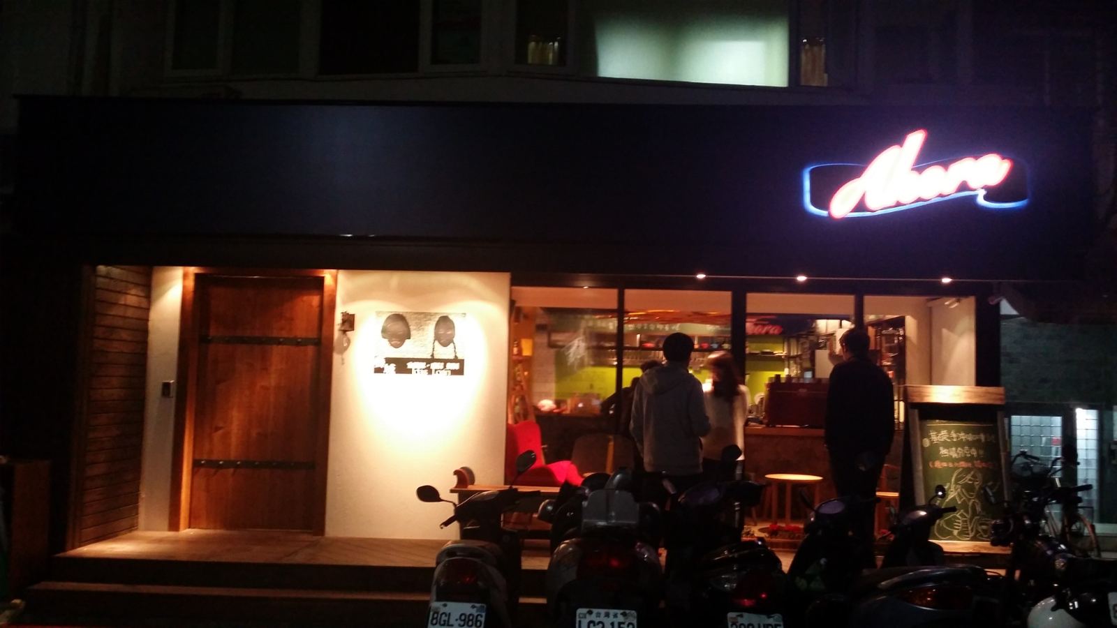 商業空間外觀展現個性風格，深黑色門頭搭配醒目的復古霓虹燈招牌，透過落地清玻璃與厚實木門營造虛實交錯的夜間立面視覺。