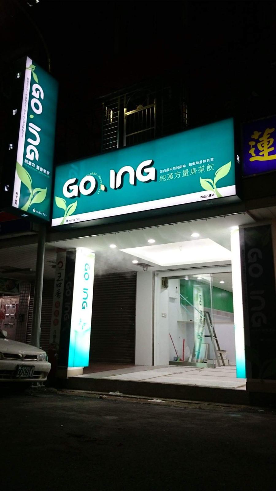 商業空間店面外觀採用青綠色與白色品牌發光燈箱，騎樓天花板配置嵌入式筒燈，搭配通透的玻璃落地門面設計。