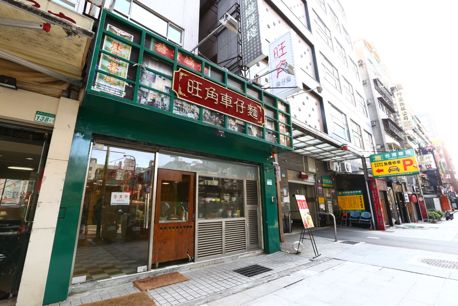 商業空間店面外觀採用墨綠色框架與復古霓虹燈箱招牌，搭配大面積通透玻璃落地窗、深色木質出入門扇及金屬百葉格柵，營造鮮明的街邊餐飲立面。