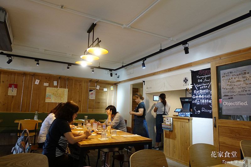 日系風格的商業餐飲空間，以暖木色與白色為主調，牆面運用大面積木質壁板與暖簾配置，搭配明管軌道燈與金屬吊燈營造質樸氛圍。