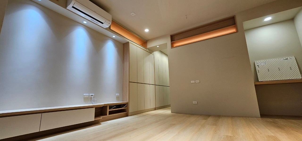 客廳空間展現現代簡約與日系無印風格，以淺木質地板搭配暖白色立面。配置俐落平整的無把手收納櫃與低矮電視櫃，結合天花板崁燈與間接燈光營造乾淨明亮的起居氛圍。