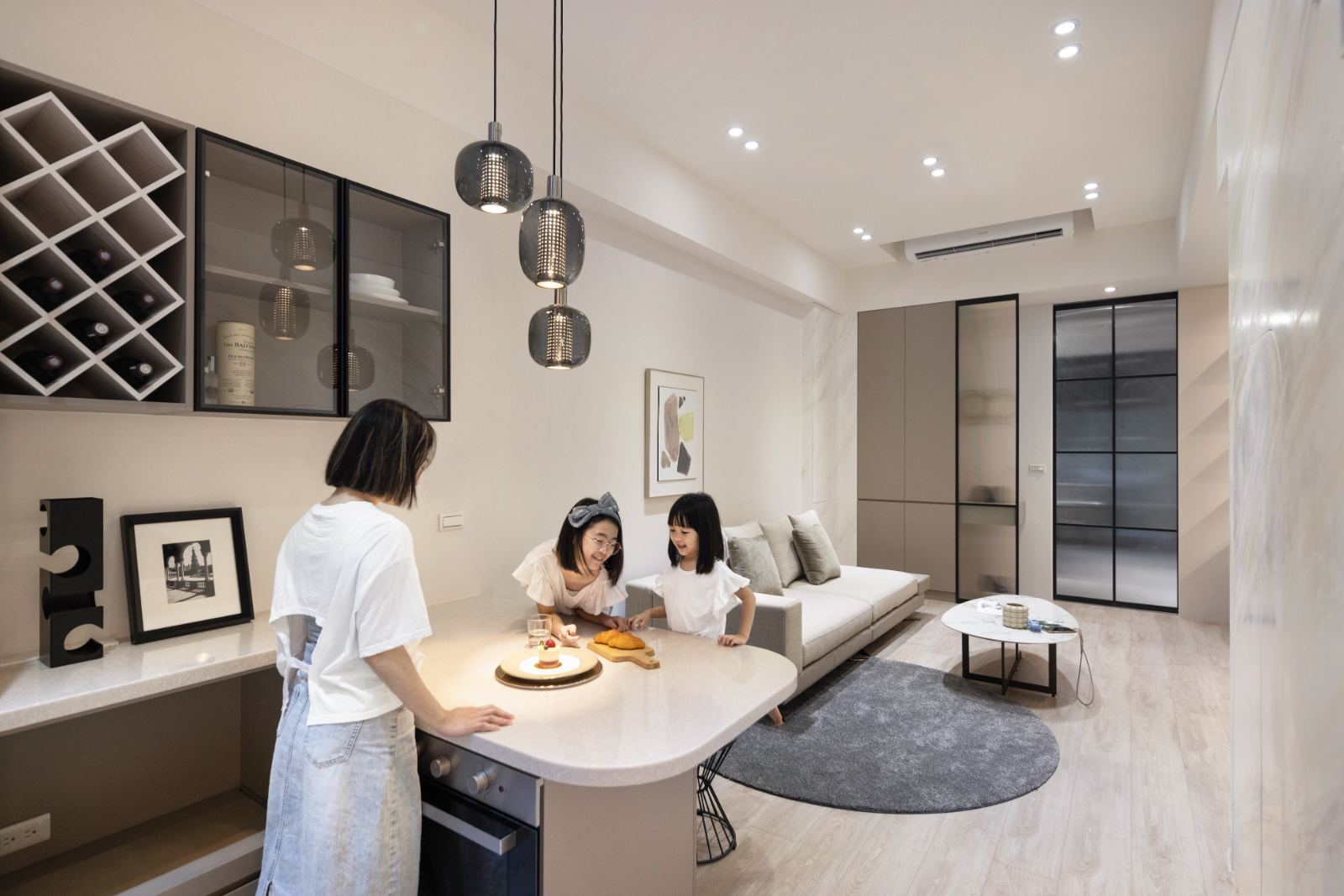 客餐廳合一的現代簡約空間，以暖白與淺灰色調為基底並鋪設淺色木地板。空間配置圓弧收邊的中島吧台與黑框玻璃吊櫃，搭配黑框拉門串聯流暢動線。