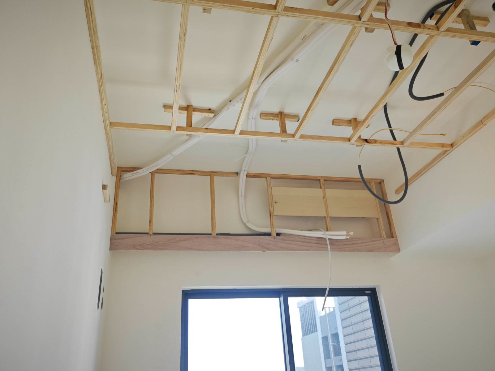 室內空間天花板施工中，以木作角材搭建吊頂骨架並預埋冷氣管線與電線，下方窗台上方施作假樑木結構，記錄裝修基礎工程狀態。