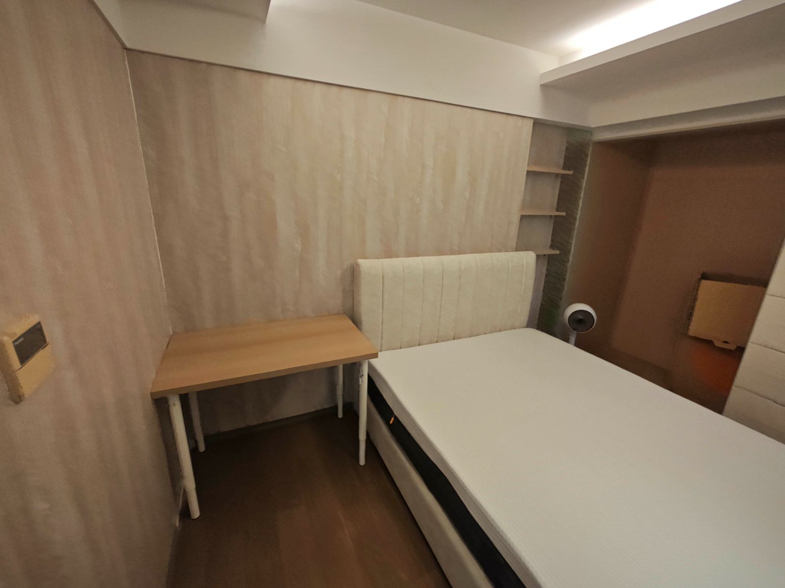 臥室呈現奶油侘寂風格，床頭背牆選用米杏色特殊塗料並以天花間接照明洗光，搭配直紋布藝床頭板與開放式層架，構築出柔和且帶有質樸肌理的空間。