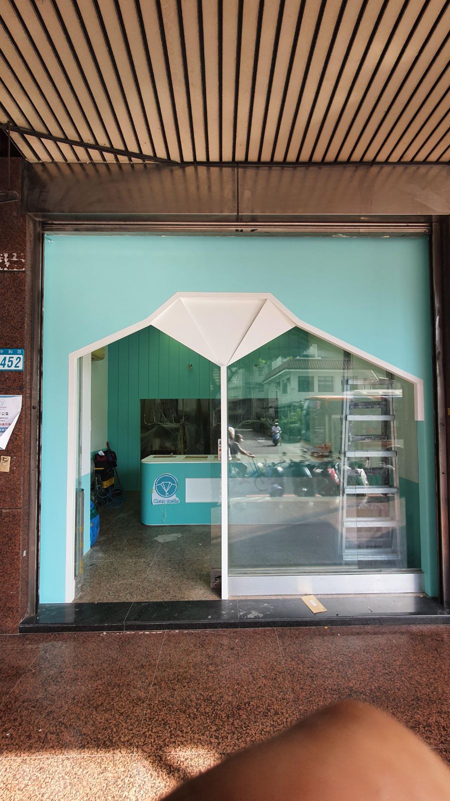 商業空間門面採用鮮明的薄荷綠塗料，結合襯衫幾何造型門框與大面通透玻璃拉門，內部配置同色系的圓弧接待櫃檯。