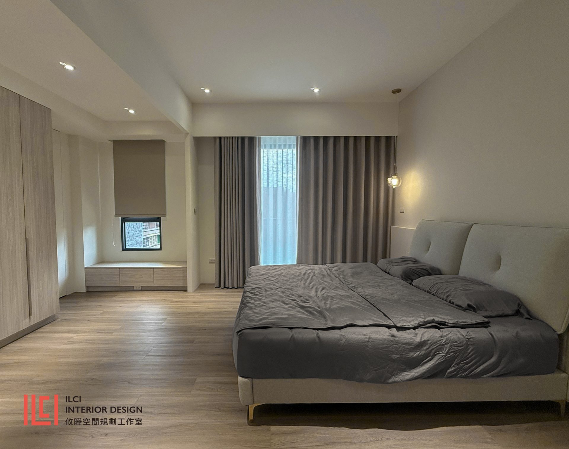 主臥室採用現代簡約風格規劃,地面鋪設溫潤木地板並搭配暖灰與米色調。窗邊配置整合抽屜收納的休閒臥榻,結合平整天花嵌燈與床頭吊燈營造純淨俐落感。